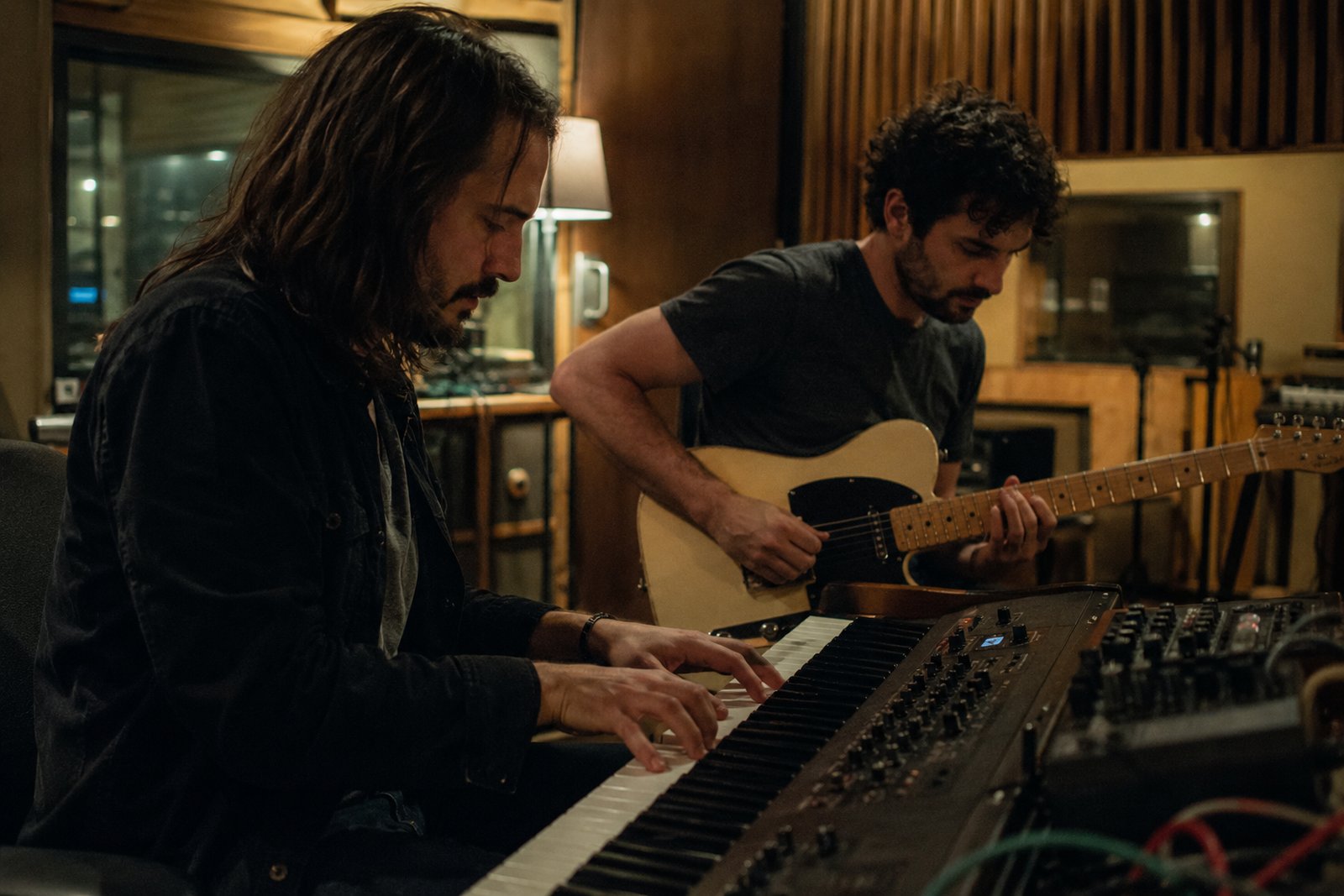 Two musicians sharing headphones at a mixing desk, listening back to a track they made together.