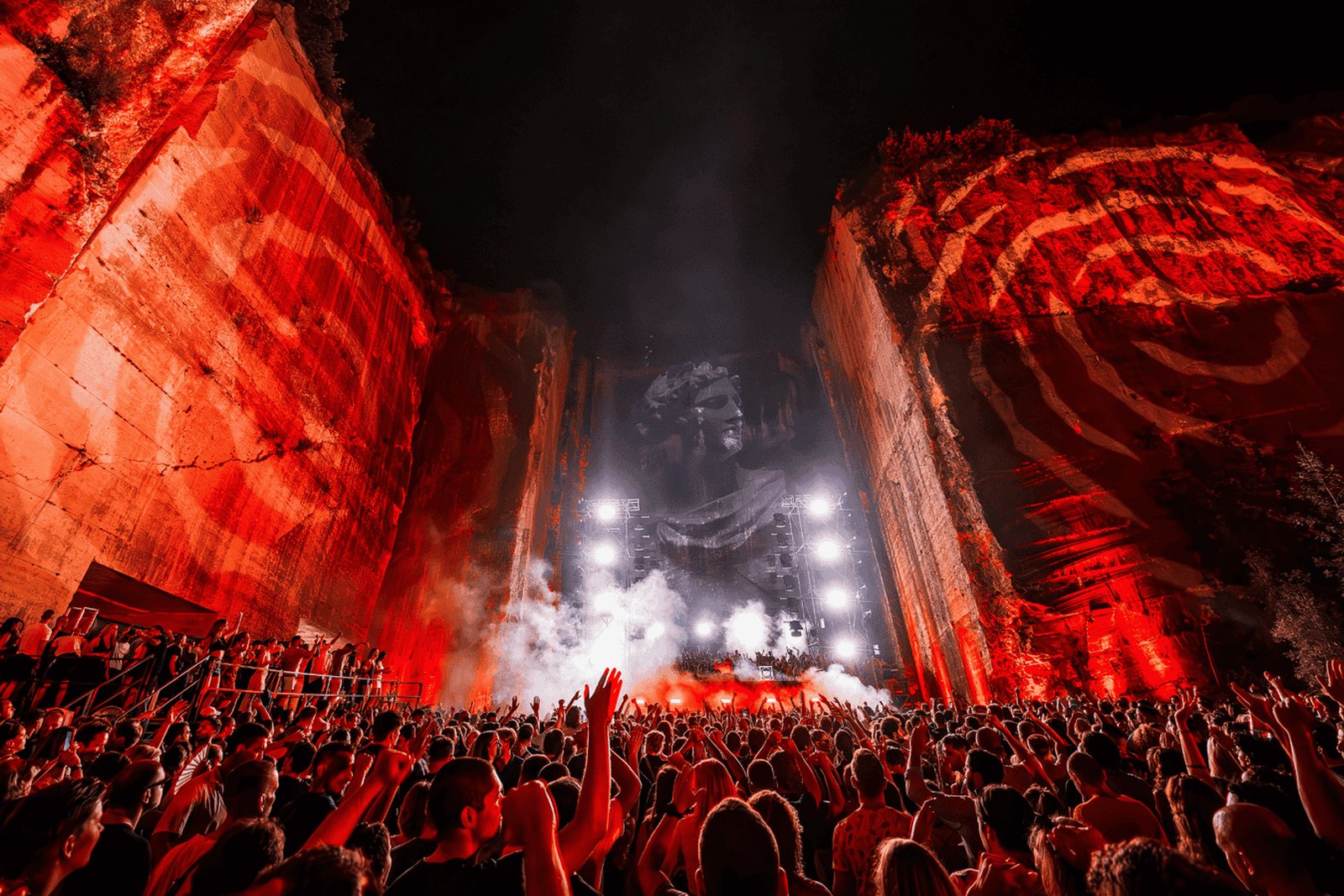 Cave Romane quarry venue at night with limestone walls lit in red and a crowd facing the stage