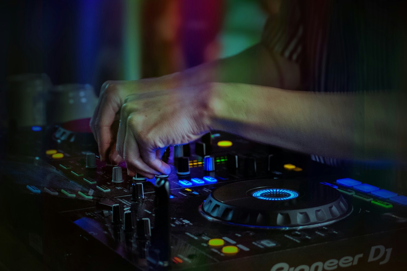 A DJ mixing on club equipment in a dark room, hands on the controls under low light.