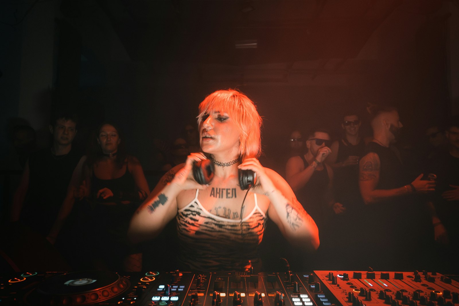 A DJ playing music behind the decks in a dimly lit nightclub
