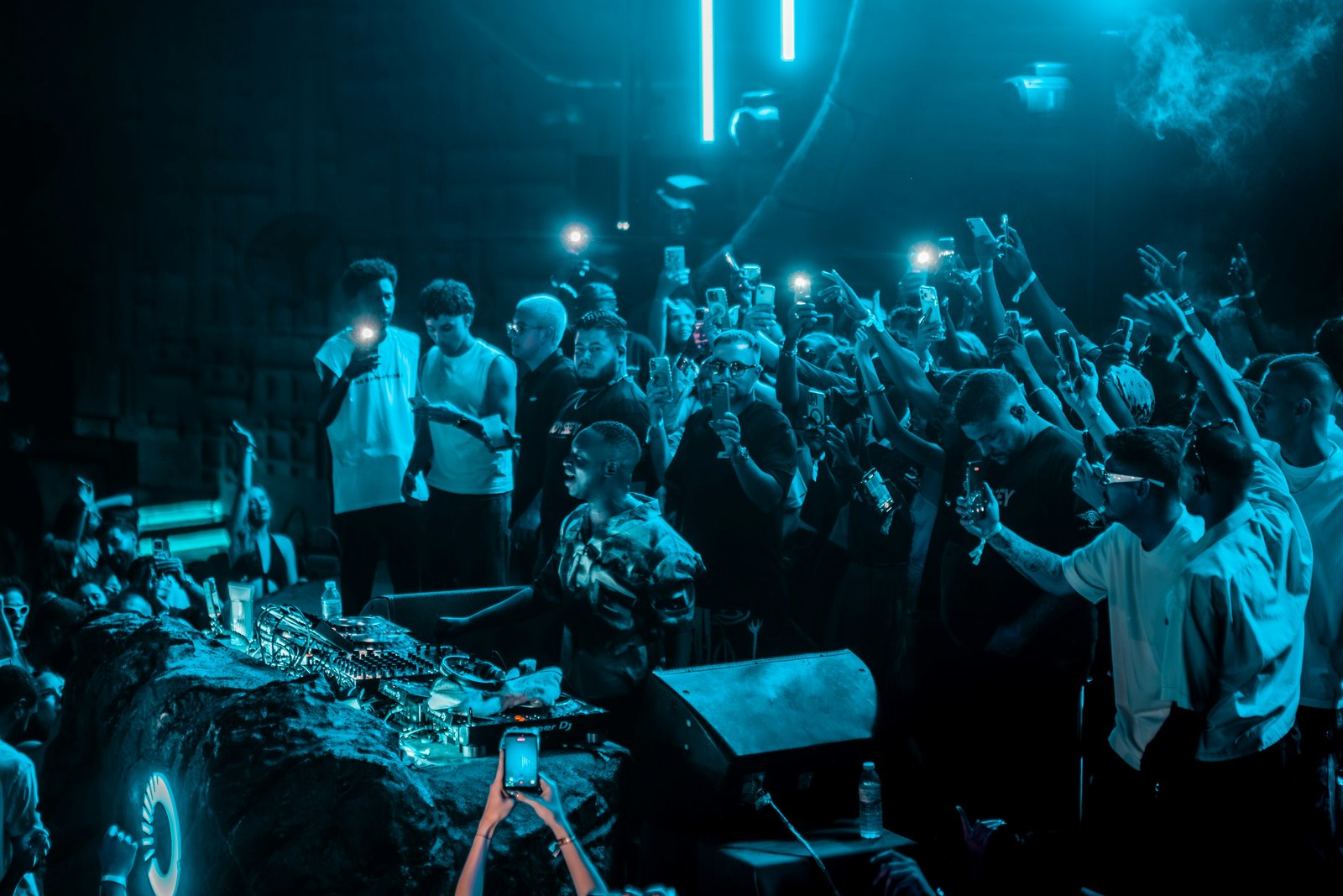 A concert crowd holding up smartphones under bright blue stage lights.
