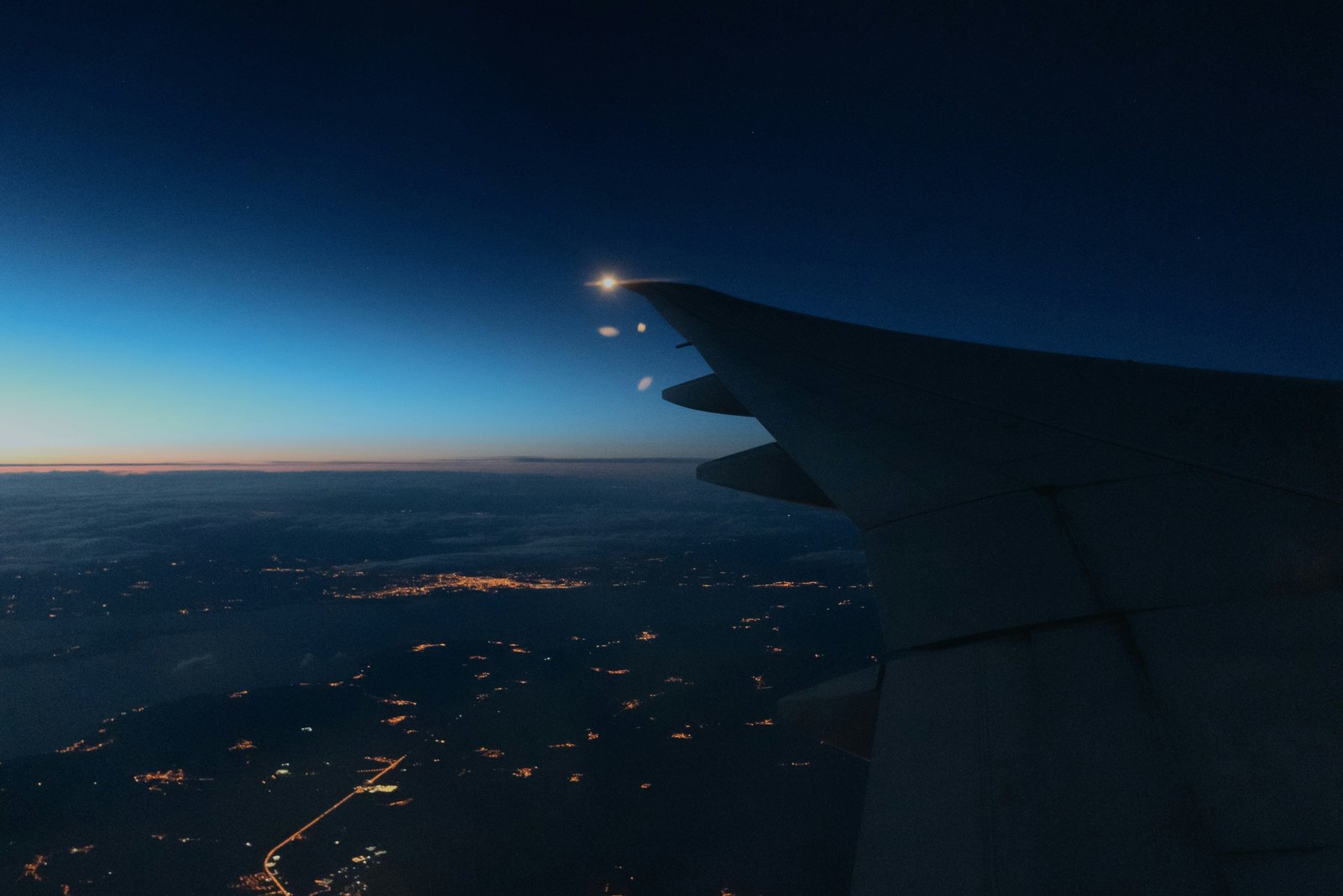 A city at night seen from an airplane window, streets and buildings glowing under blue-toned light.