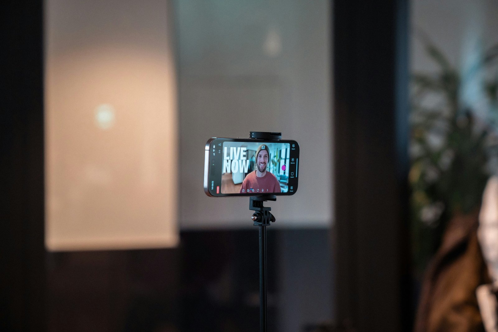 A smartphone mounted on a tripod records a person in a room lit with cool blue and teal tones.