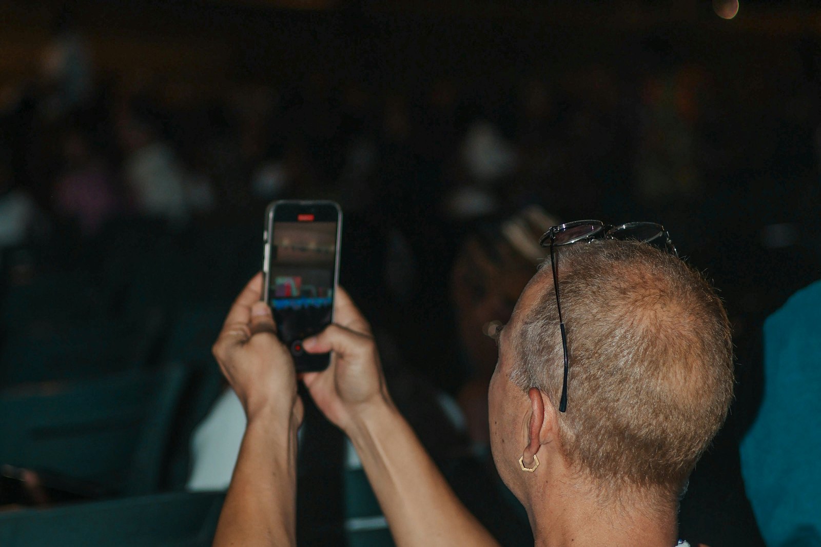 A man holding up a smartphone to film an outdoor event at night.