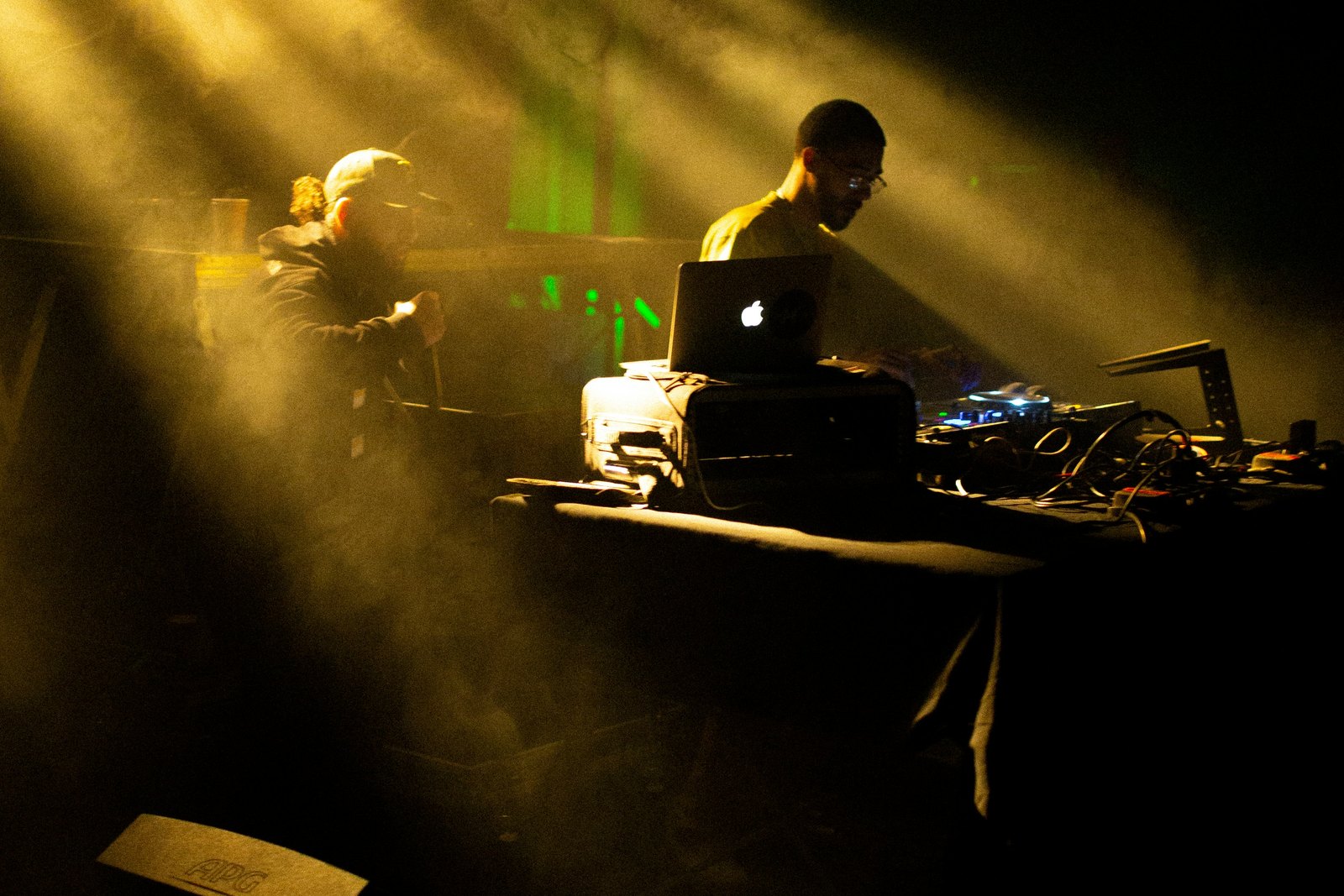 A DJ performing on a stage in front of a crowd of people under coloured lights