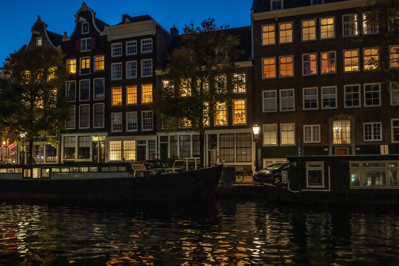 Amsterdam canal houses lit up at dusk with their lights reflected in the water