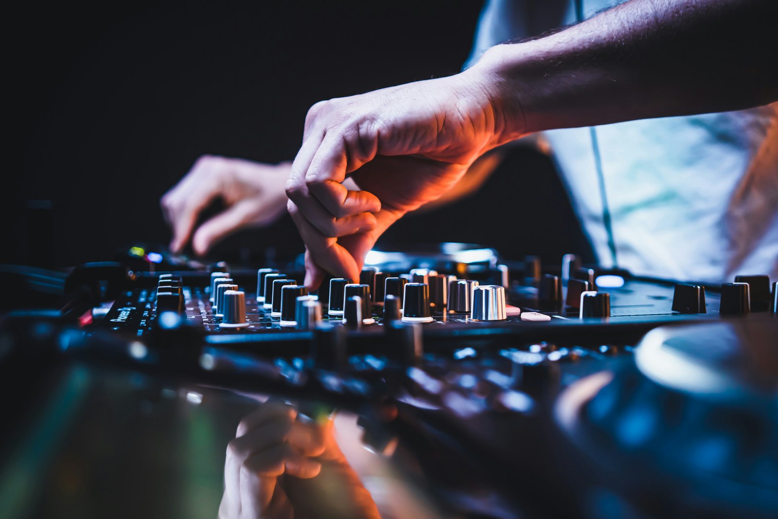 Close up of a person's hands on a DJ mixer in a club under coloured lights.