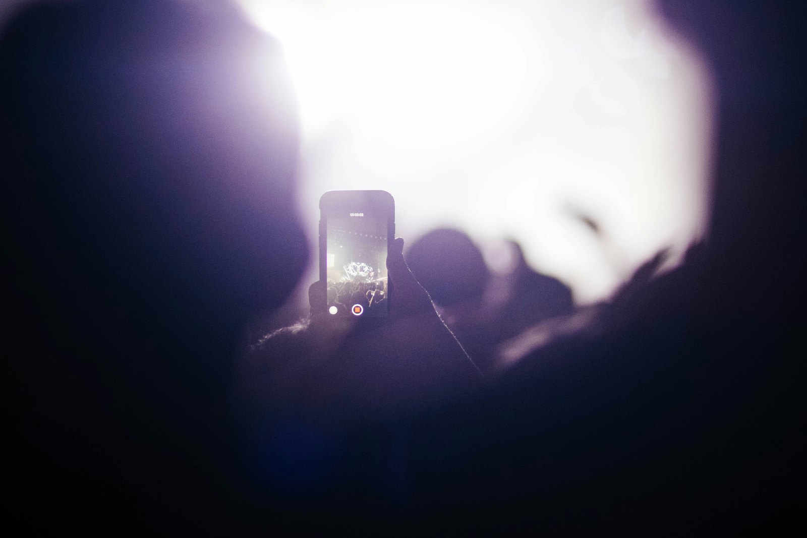 A person holding up a smartphone to record video in a dark setting at night