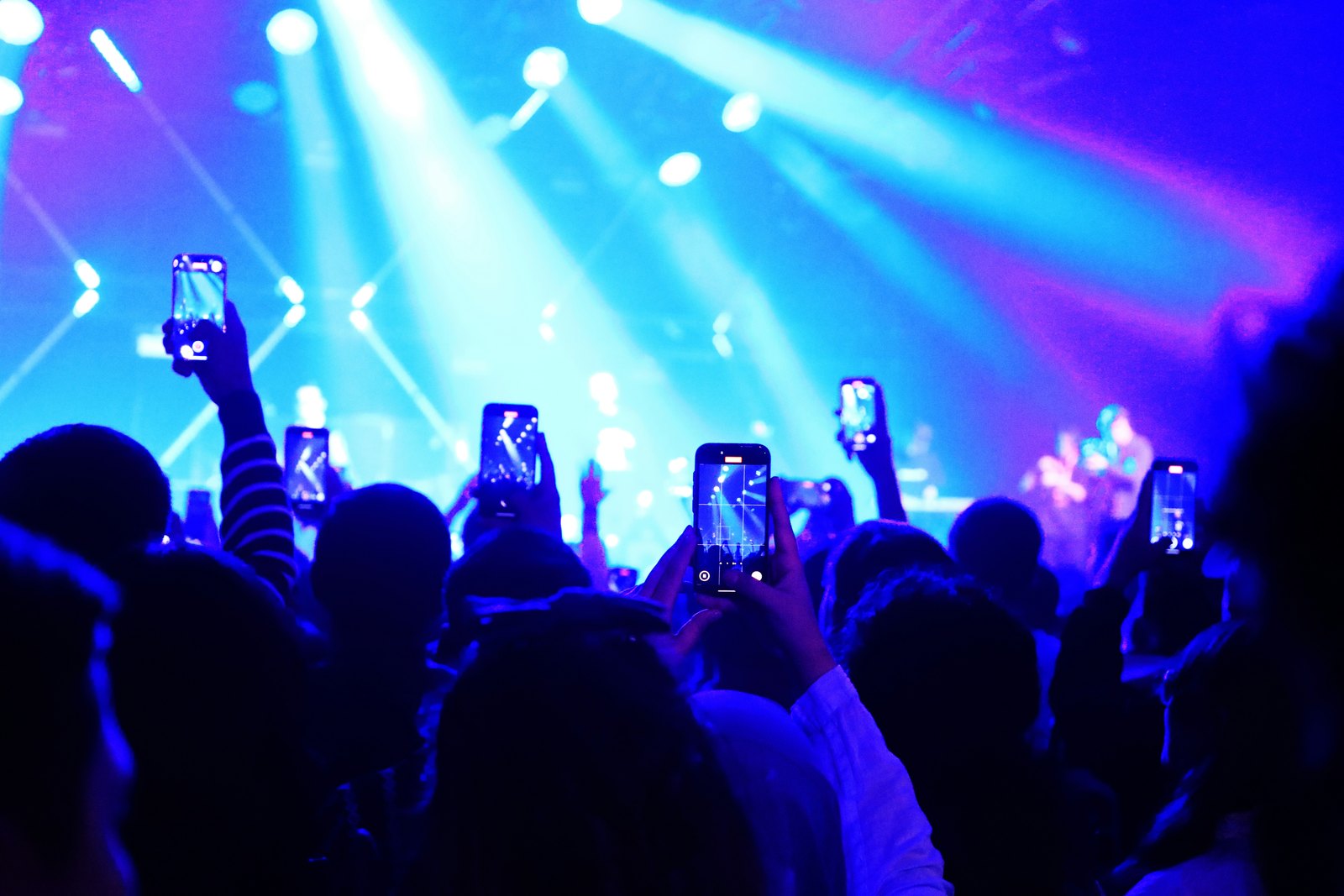 A concert crowd in deep blue light, with many people holding up their phones to record the stage.