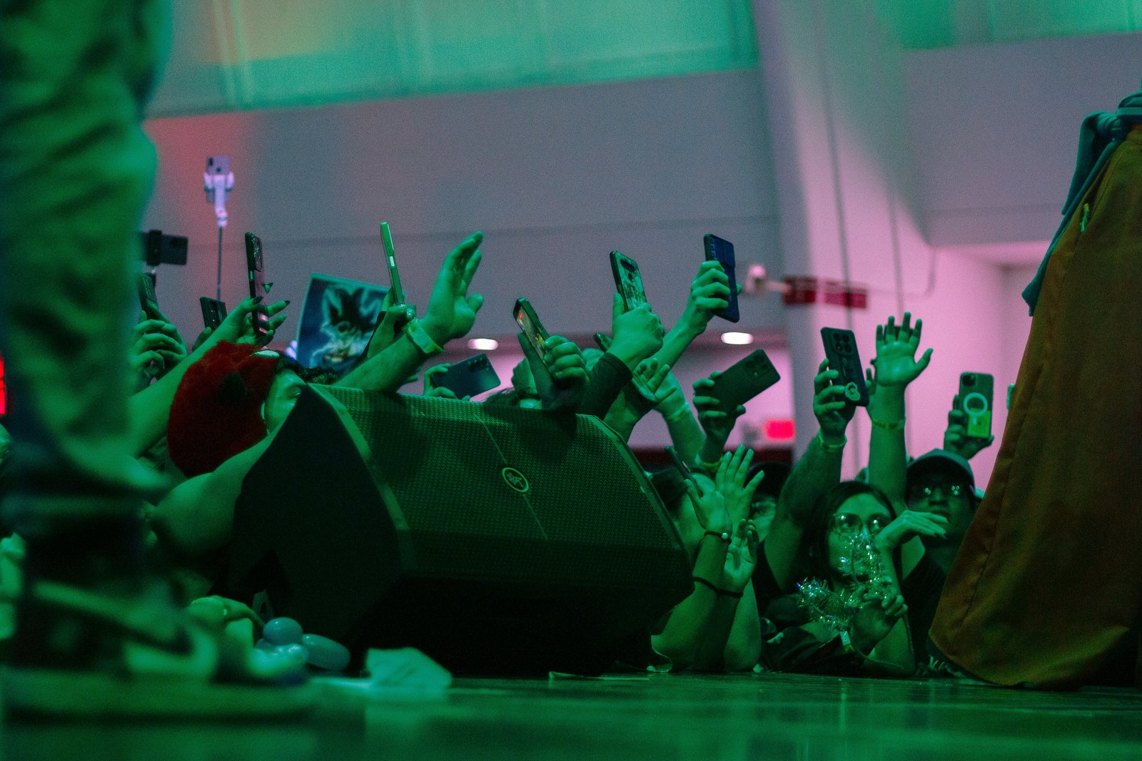 A crowd at a concert with hands raised, holding up smartphones to film the stage