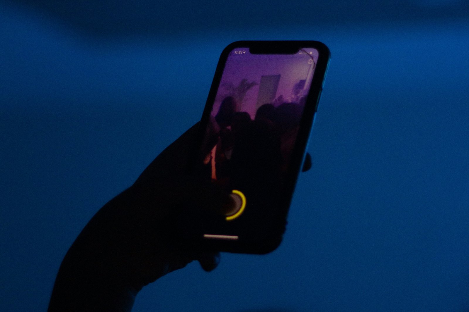 A person holding up a glowing mobile phone in a dark room