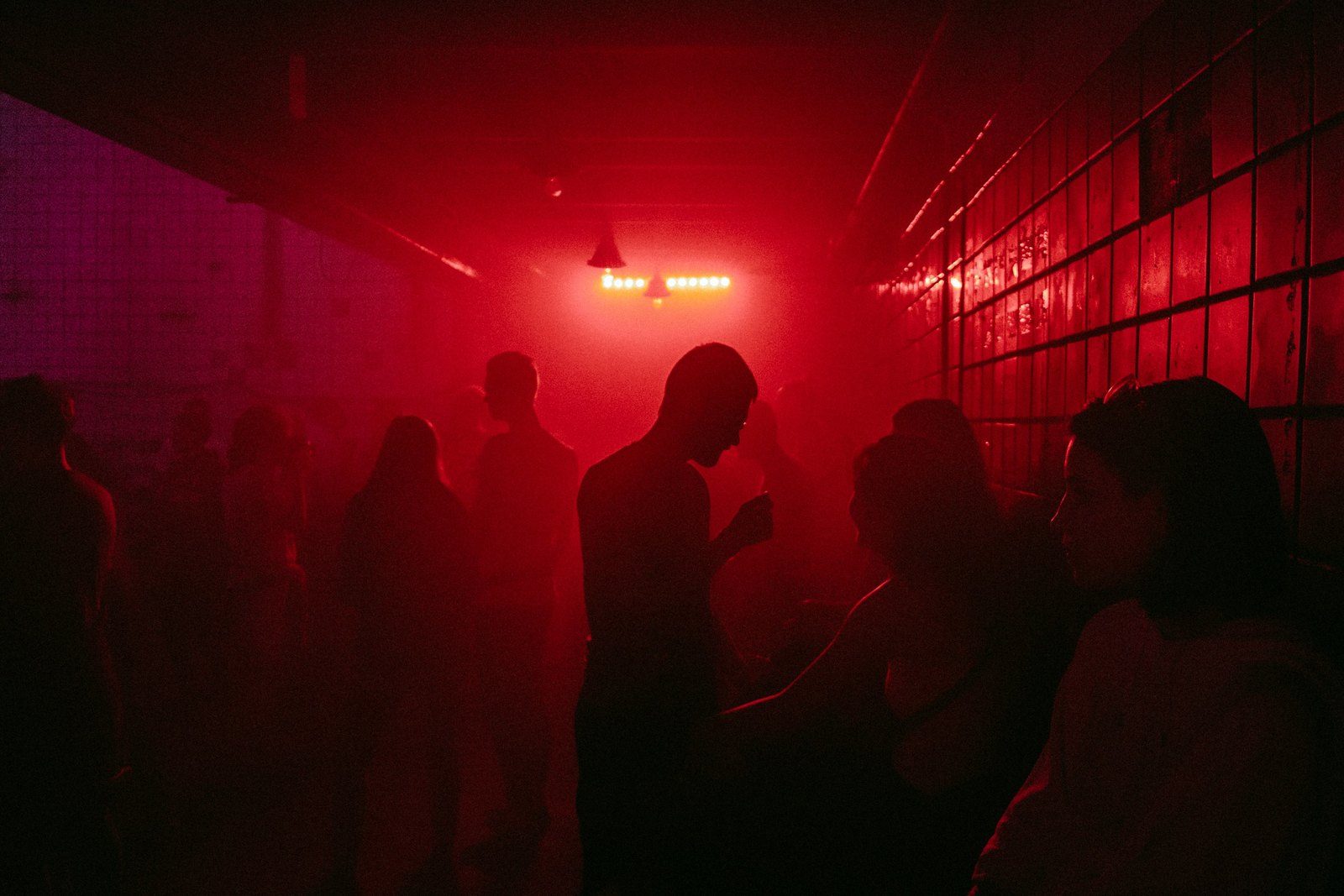 Silhouettes of people on a dark club floor, backlit by intense red light.