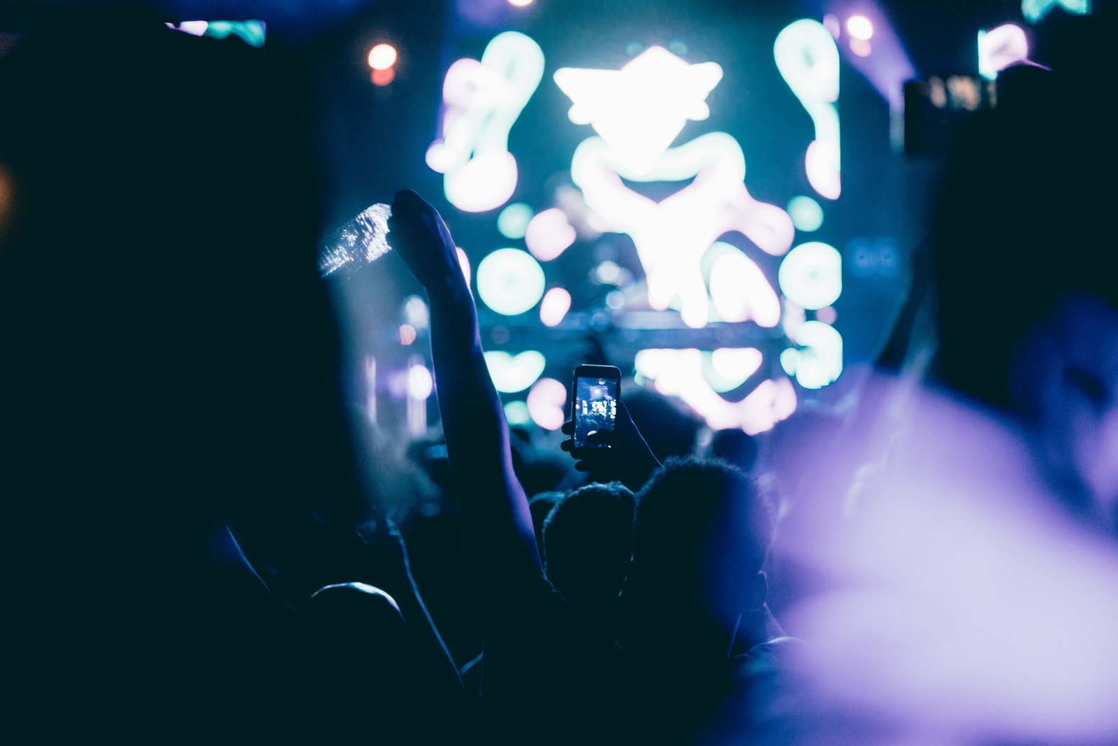 A concert crowd in blue stage light holding up their phones to film the performance.
