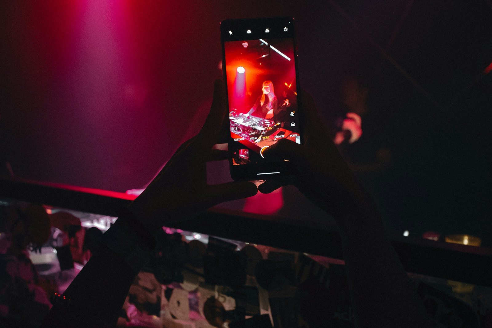 A smartphone held up to record a live performance under deep red and orange stage lights.