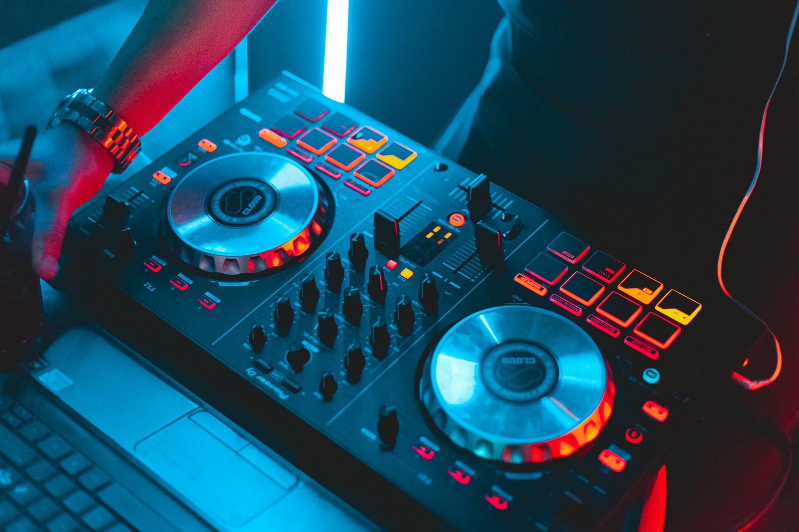 A black DJ controller with its buttons and pads lit up, sitting in a dim, dark room.