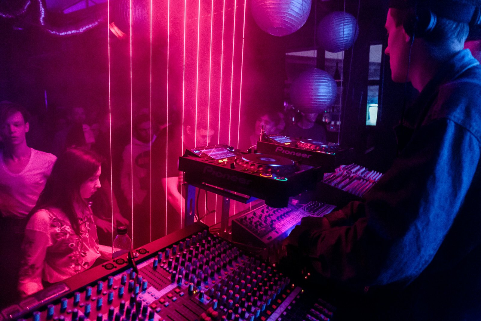 A DJ mixing music in a dark room, lit by low coloured light.