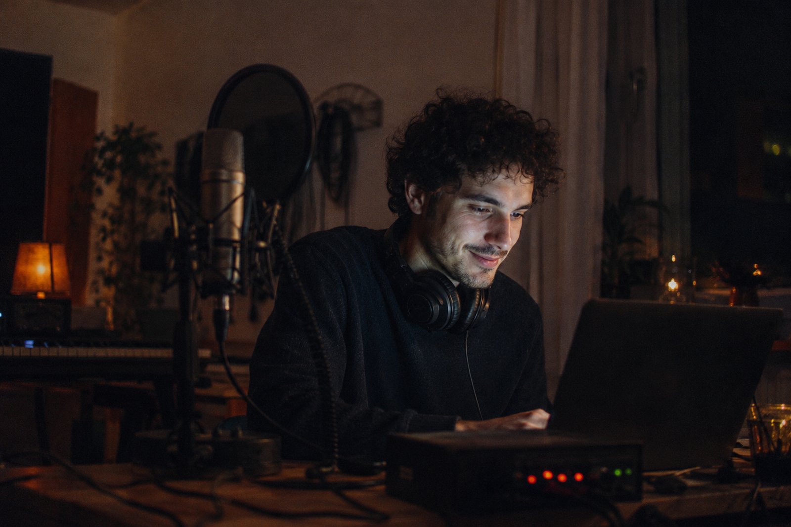 Artist at a laptop in a home studio at night talking with fans, warm screen glow