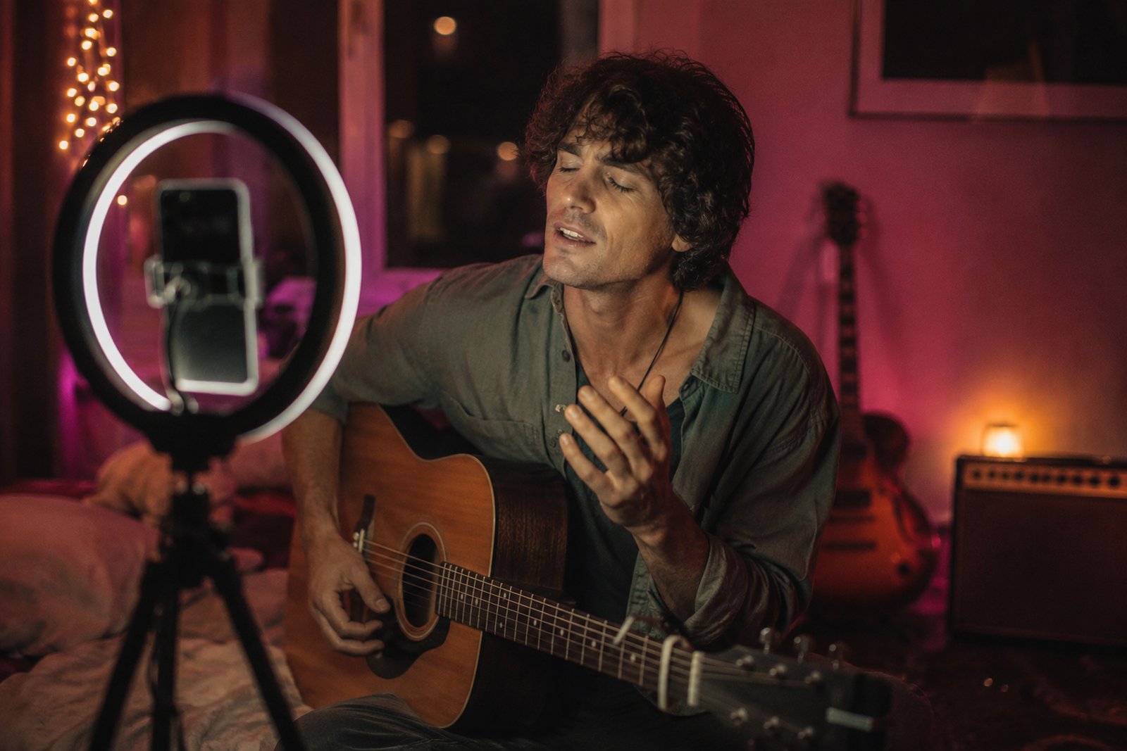 Artist performing to a phone on a tripod ring light in a bedroom studio at night